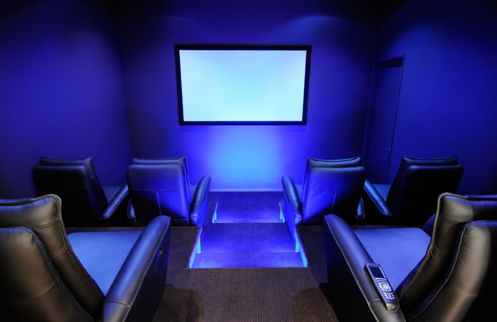 Sala de cinema montada em casa, com luzes de led azul, poltronas e tela.