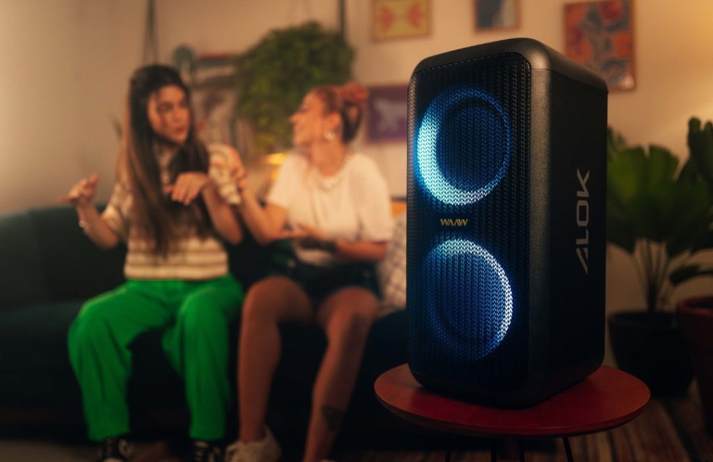 Mulheres sentadas em sofé se divertindo ouvindo música em caixa de som com led.