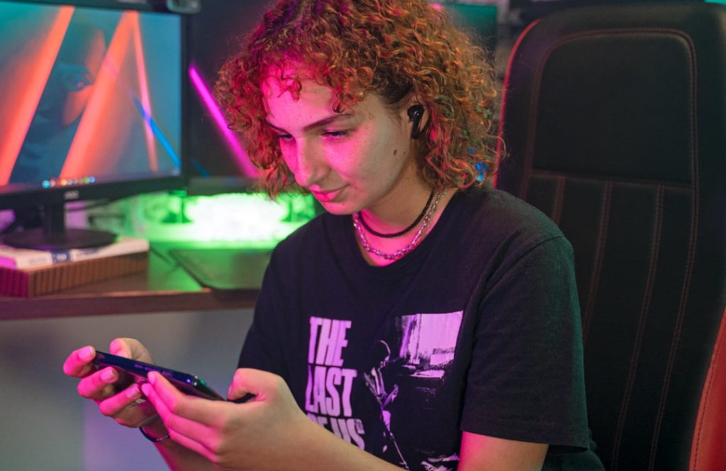 Mulher jogando jogo em celular com o fone de ouvido da WAAW by Alok.